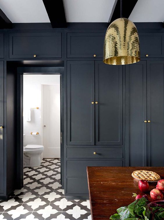 Blue-black cabinets, a hammered brass pendant, a wooden island and black and white tiles make a memorable impression in this kitchen. | Photographer: Amy Bartlam | Designer: Jette Creative