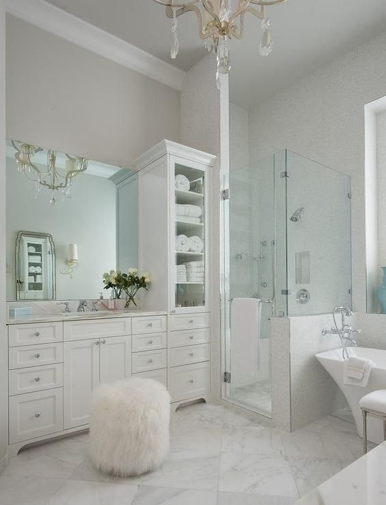 White and gray master bathroom features walls painted soft, creamy gray lined with white vanity cabinets topped with white marble under a frameless mirror situated next to a tall mirrored linen cabinet.