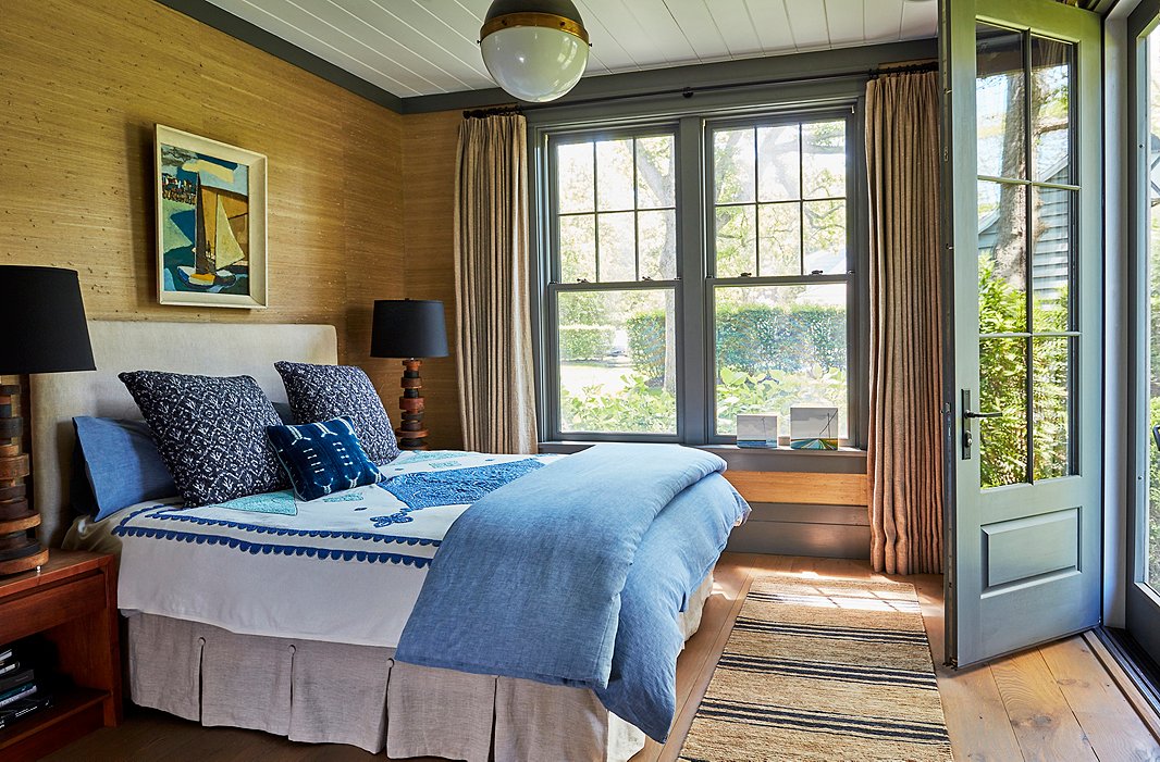 AÂ painting from a flea market in Saint-Tropez crowns a linen-upholstered bed. Soft gray trim frames the seagrass-covered walls, while mismatched bedding in shades of indigo reflects the hues of Wooley Pond.